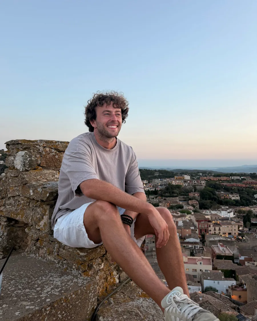 Martin, smiling, sitting on an old stone wall at sunset.